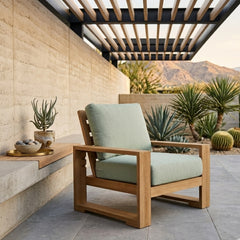 Anderson Teak Capistrano deep seating armchair in a stylish outdoor patio setting with lush garden background.